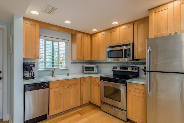 kitchen with light hardwood / wood-style floors, stainless steel appliances, light brown cabinetry, decorative backsplash, and sink