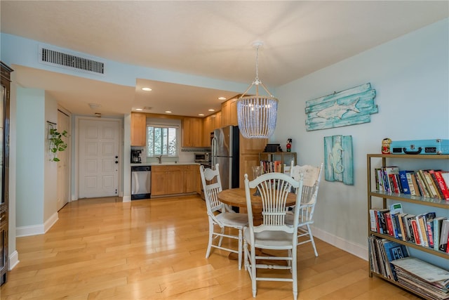 dining area with a notable chandelier, light wood-type flooring, and sink