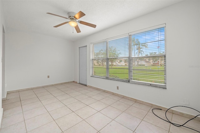 tiled empty room with a textured ceiling, a wealth of natural light, and ceiling fan