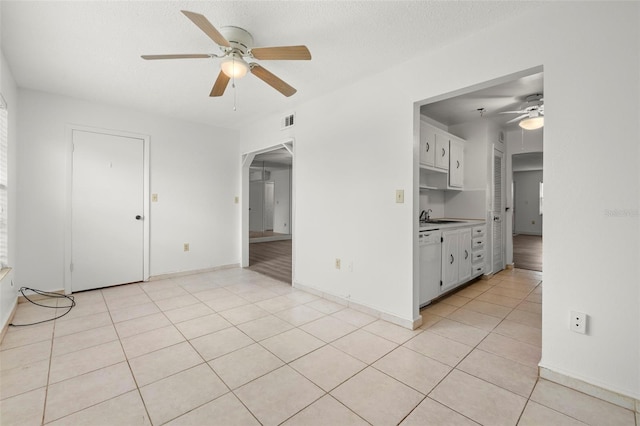 interior space with a textured ceiling, white dishwasher, sink, light tile patterned floors, and white cabinetry