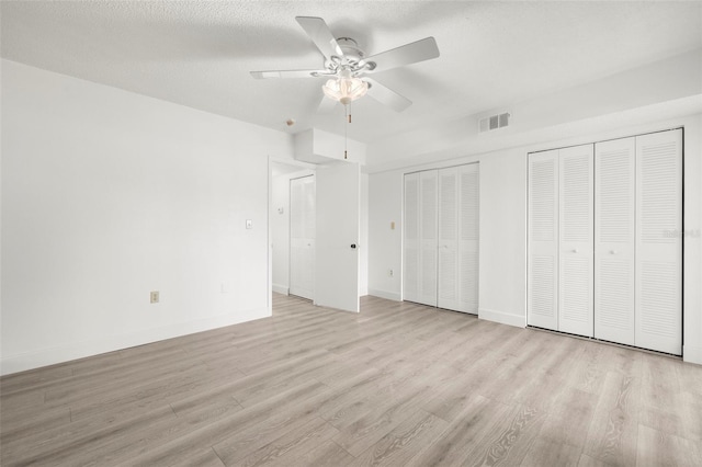 unfurnished bedroom featuring ceiling fan, light hardwood / wood-style floors, a textured ceiling, and multiple closets