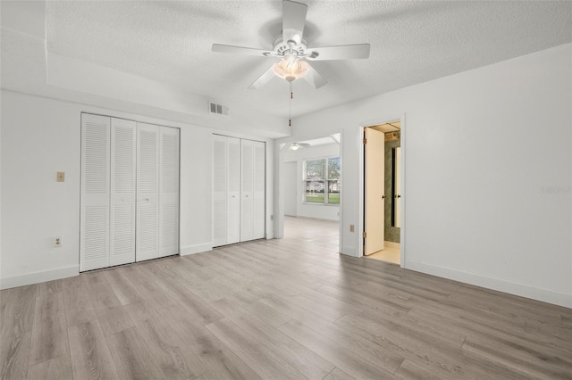 unfurnished bedroom with a textured ceiling, light wood-type flooring, ensuite bath, and ceiling fan