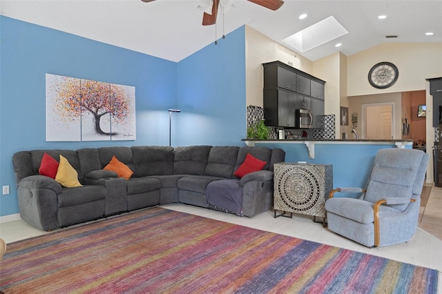 living room with high vaulted ceiling, a skylight, and ceiling fan