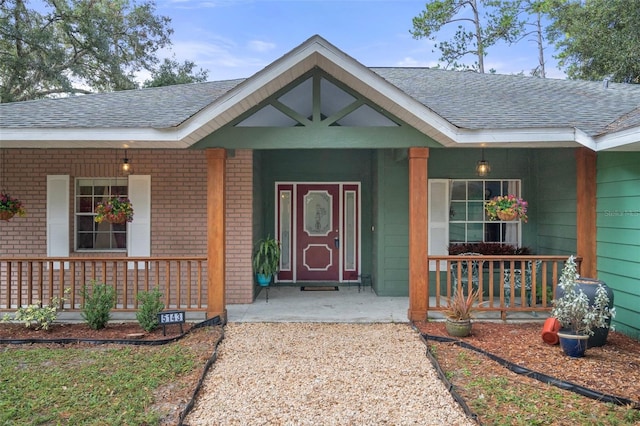 entrance to property featuring brick siding, a porch, and a shingled roof