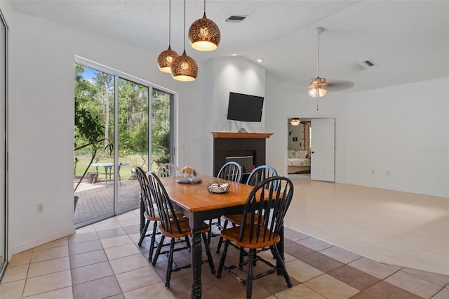 dining space with light tile patterned flooring, vaulted ceiling, visible vents, and a glass covered fireplace
