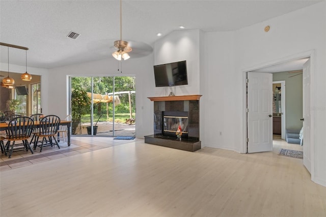 living area with a textured ceiling, visible vents, a fireplace, wood finished floors, and a ceiling fan