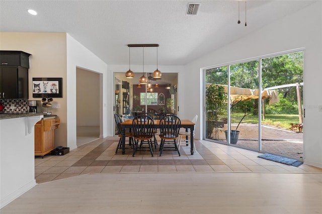 dining room with light tile patterned floors, a textured ceiling, lofted ceiling, and visible vents