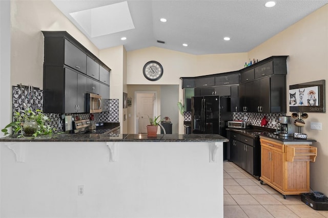 kitchen featuring light tile patterned flooring, a peninsula, a kitchen bar, stainless steel microwave, and dark cabinetry