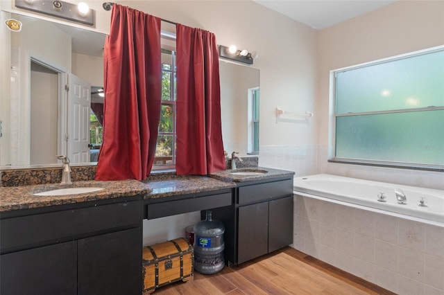 bathroom with double vanity, wood finished floors, a sink, and a garden tub