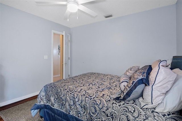 bedroom with a textured ceiling, visible vents, baseboards, wood finished floors, and a ceiling fan