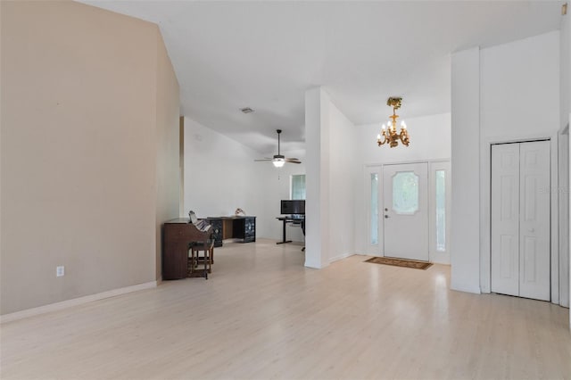 foyer with ceiling fan with notable chandelier, light wood-type flooring, high vaulted ceiling, and baseboards