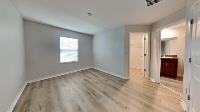 unfurnished bedroom featuring a walk in closet, a closet, sink, and light wood-type flooring