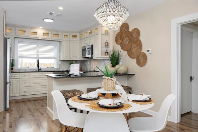 kitchen with appliances with stainless steel finishes, sink, backsplash, hanging light fixtures, and light hardwood / wood-style floors