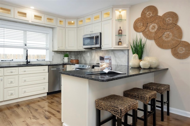 kitchen featuring kitchen peninsula, stainless steel appliances, sink, a kitchen bar, and tasteful backsplash