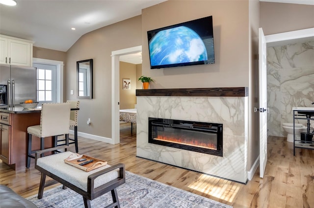 living room with a premium fireplace, light wood-type flooring, and vaulted ceiling