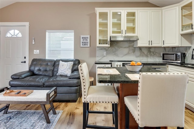 kitchen with lofted ceiling, stainless steel appliances, backsplash, a kitchen bar, and white cabinetry