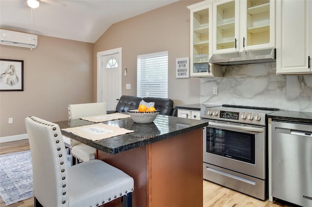 kitchen featuring light wood-type flooring, backsplash, stainless steel appliances, a wall unit AC, and a breakfast bar