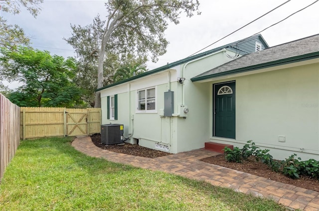 entrance to property featuring electric panel, a lawn, and cooling unit