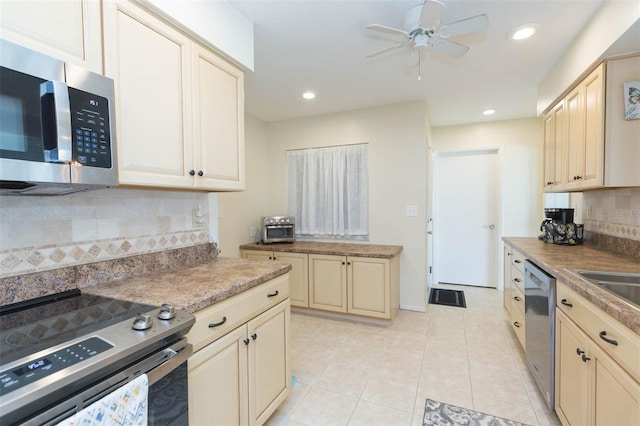 kitchen with appliances with stainless steel finishes, cream cabinets, backsplash, ceiling fan, and light tile patterned floors