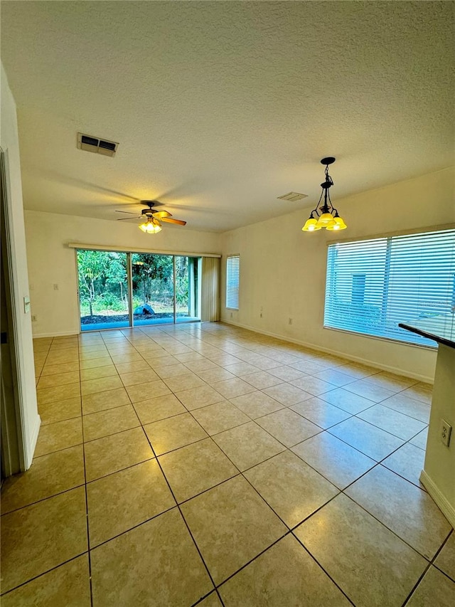 tiled spare room with a textured ceiling and ceiling fan with notable chandelier