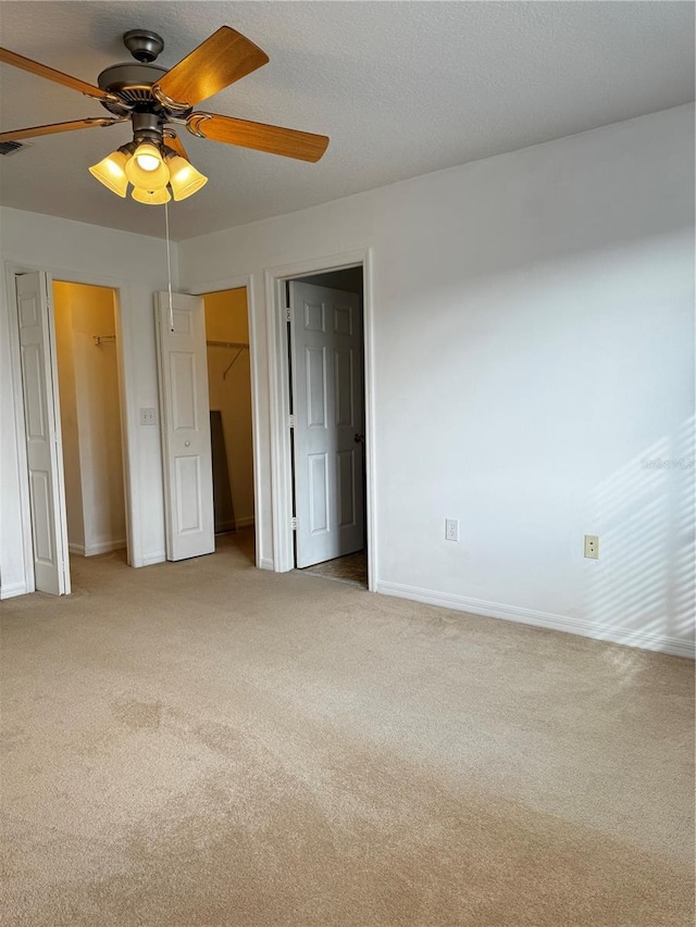 unfurnished bedroom with light colored carpet, ceiling fan, a textured ceiling, and baseboards