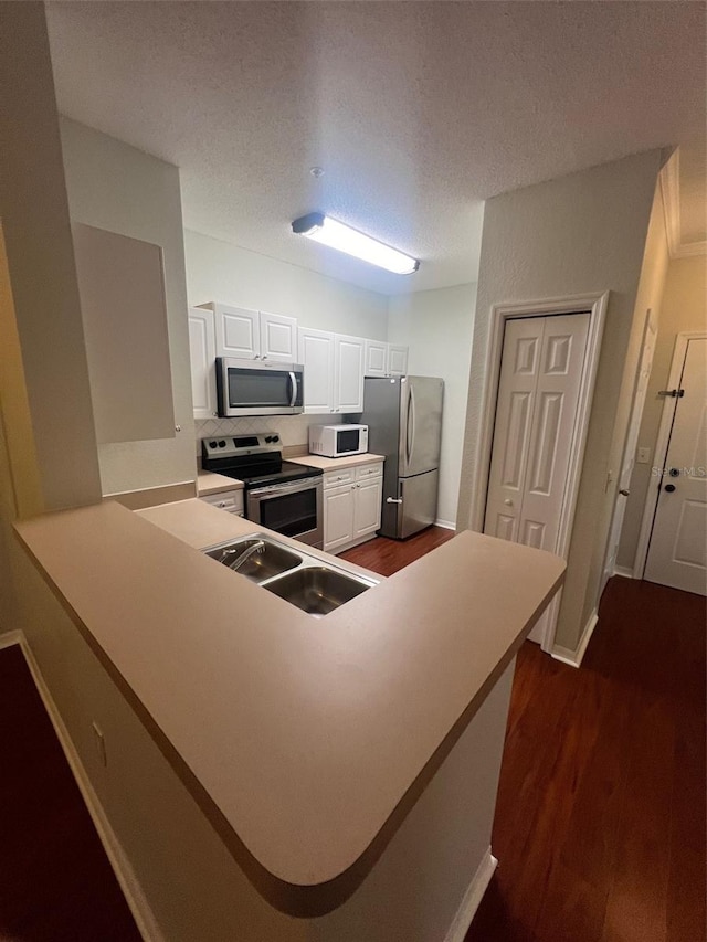 kitchen with stainless steel appliances, sink, kitchen peninsula, white cabinets, and dark hardwood / wood-style flooring