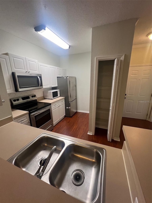 kitchen with appliances with stainless steel finishes, a textured ceiling, sink, white cabinets, and dark wood-type flooring