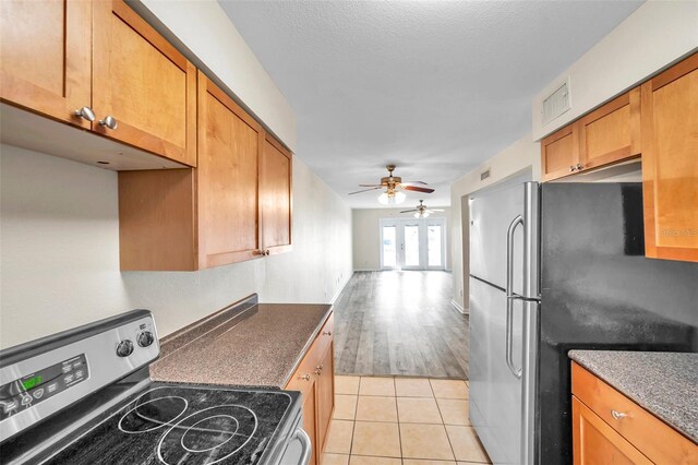 kitchen with ceiling fan, a textured ceiling, stove, stainless steel refrigerator, and light hardwood / wood-style floors