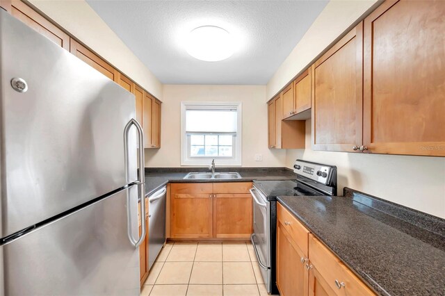 kitchen with sink, a textured ceiling, stainless steel appliances, dark stone counters, and light tile patterned floors