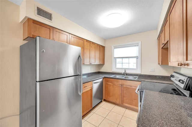 kitchen with light tile patterned floors, a textured ceiling, appliances with stainless steel finishes, and sink