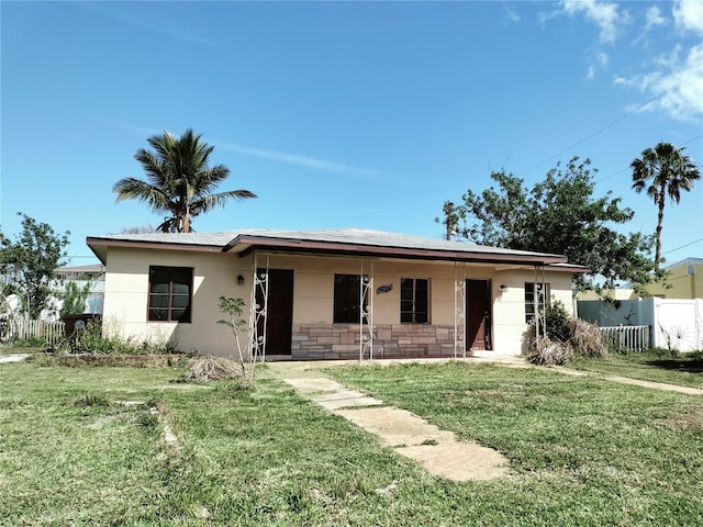 single story home featuring covered porch, stone siding, fence, and a front yard