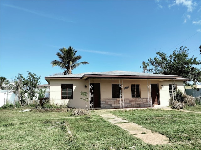 view of front of property with stucco siding, a porch, a front yard, fence, and stone siding