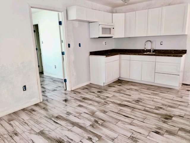 kitchen with dark countertops, white microwave, white cabinets, and a sink