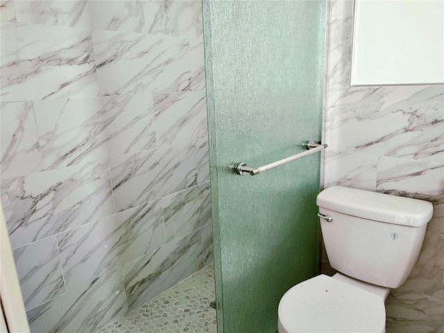 bathroom with toilet, a stall shower, and tile walls