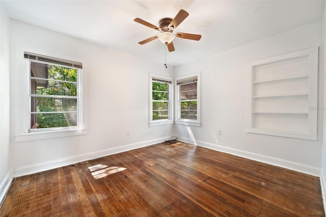 spare room featuring a wealth of natural light, ceiling fan, built in shelves, and hardwood / wood-style flooring