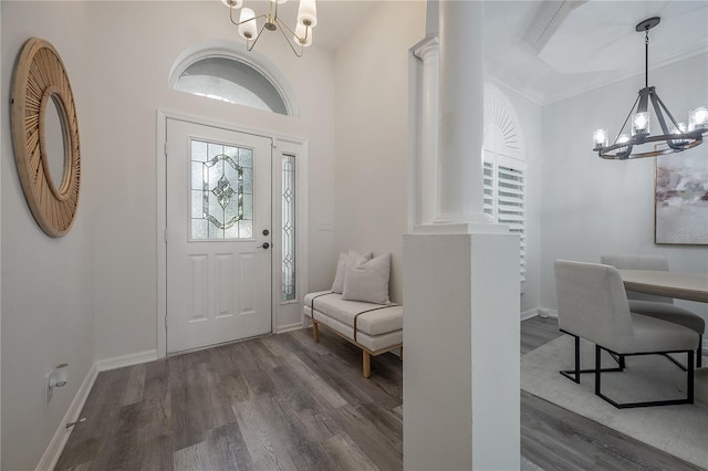 foyer entrance featuring dark wood-type flooring, ornate columns, ornamental molding, and a chandelier