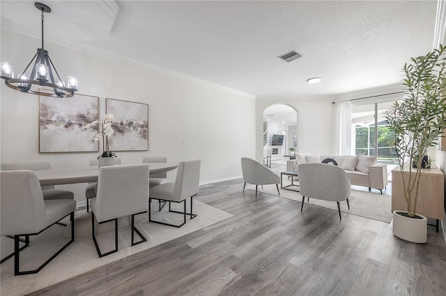 dining space with hardwood / wood-style flooring, ornamental molding, an inviting chandelier, and a textured ceiling