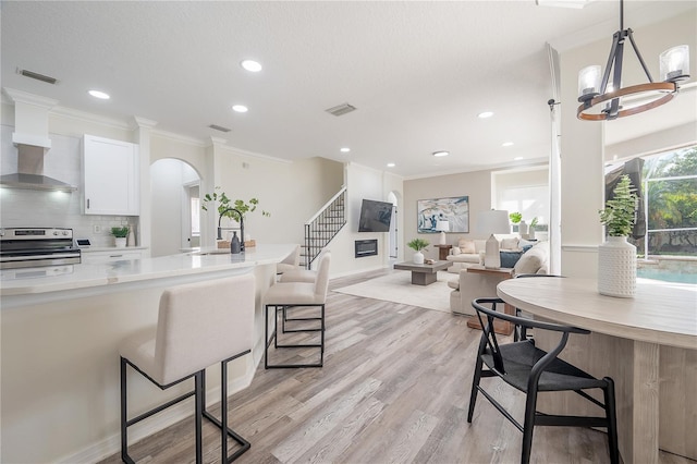 kitchen with white cabinets, a breakfast bar, stainless steel stove, light hardwood / wood-style flooring, and decorative light fixtures