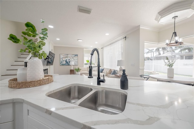 kitchen featuring an inviting chandelier, crown molding, sink, and light stone counters