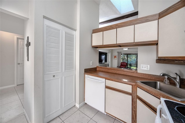 kitchen with white appliances, a skylight, sink, white cabinetry, and light tile patterned floors