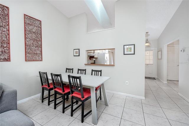 dining area featuring high vaulted ceiling, a textured ceiling, a skylight, and light tile patterned flooring