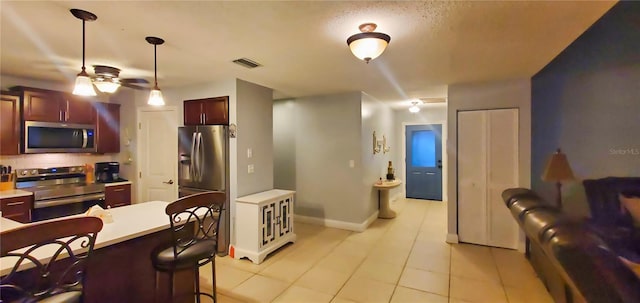 kitchen featuring light tile patterned flooring, a kitchen breakfast bar, ceiling fan, stainless steel appliances, and decorative light fixtures