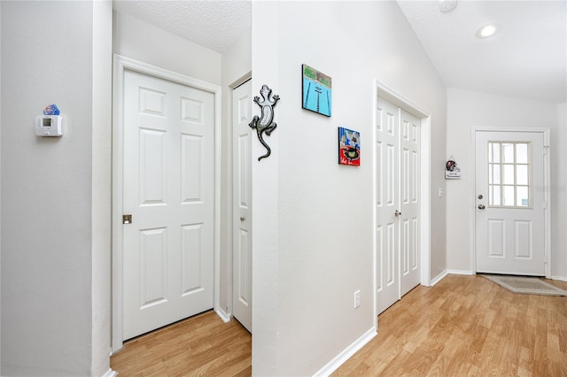 foyer entrance with lofted ceiling, a textured ceiling, and light hardwood / wood-style floors