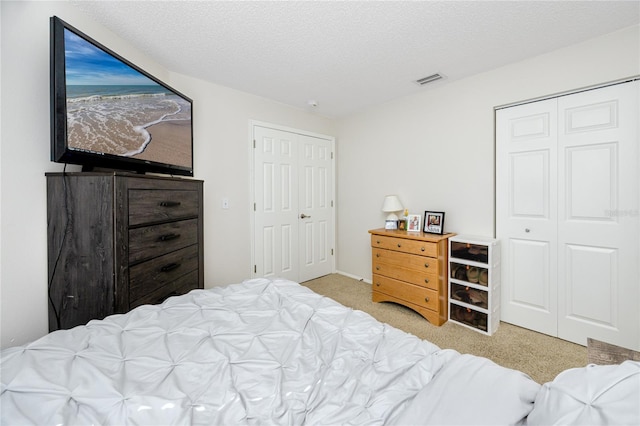 bedroom featuring a textured ceiling, two closets, and light colored carpet