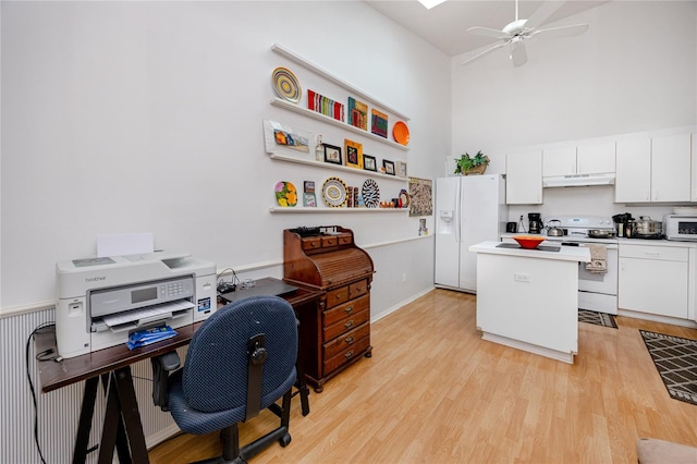 office space with a towering ceiling, light wood-type flooring, and ceiling fan