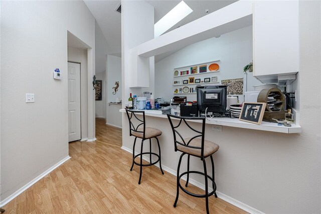 kitchen with white cabinets, light wood-type flooring, kitchen peninsula, and a kitchen breakfast bar