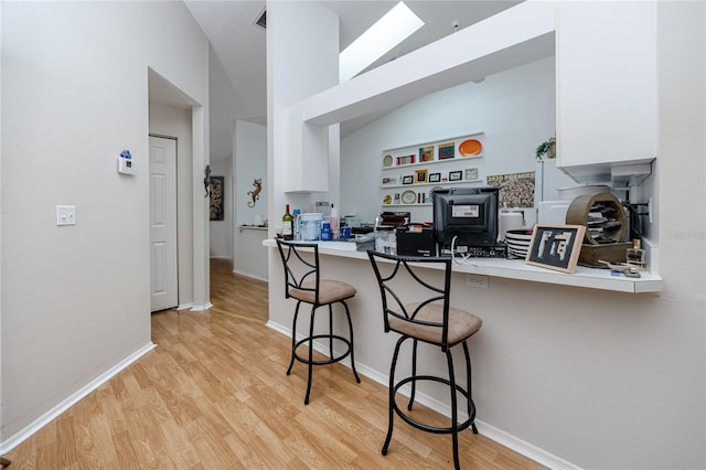 4234 Chesterfield Cir, Palm Harbor, FL 34683 - kitchen featuring a kitchen breakfast bar, light wood-style flooring, baseboards, white cabinetry, and high vaulted ceiling