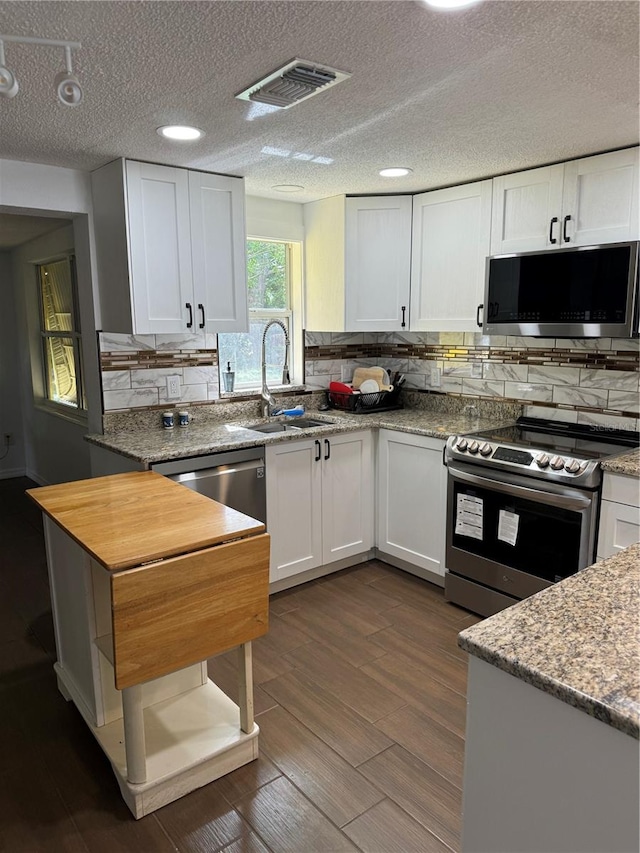 kitchen with appliances with stainless steel finishes, backsplash, dark wood-type flooring, sink, and white cabinetry