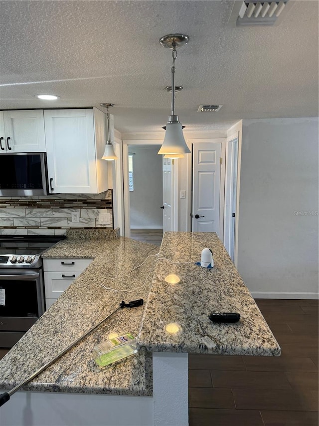 kitchen featuring appliances with stainless steel finishes, backsplash, dark hardwood / wood-style floors, white cabinetry, and hanging light fixtures