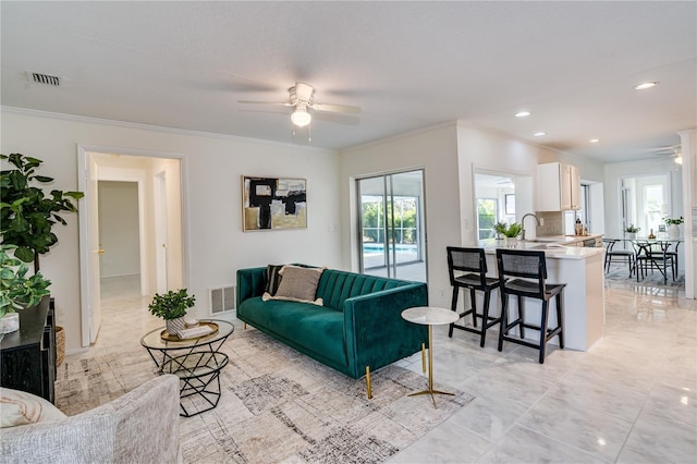 living room featuring ceiling fan, crown molding, and sink